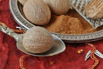 Whole nutmeg and nutmeg powder on spoon and plate