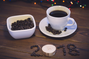 A romantic festive still life with a cup of coffee with a saucer, a bowl of coffee beans and 2018 inscription of coffee beans on a rustic wooden background.