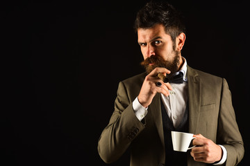 Boss with beard smokes cigar with cup of coffee