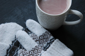 White knitted mittens and a cup of coffee on a black background.