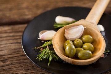 Green olives, rosemary and wooden ladle on table