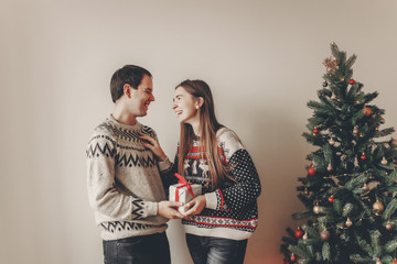 happy family in stylish sweaters exchanging gifts in festive room with christmas tree and lights....