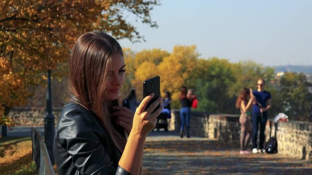 Young beautiful woman takes selfie photos in autumn park in sunny day