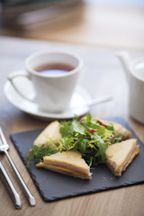 a variety of club sandwiches served in a white plate with a cup of hot tea