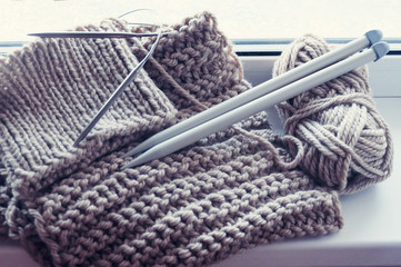 A knitted scarf with a thick thread on thick beige knitting needles. Close-up with blur.