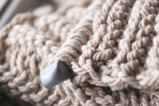 A knitted scarf with a thick thread on thick beige knitting needles. Close-up with blur.