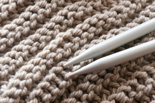 A knitted scarf with a thick thread on thick beige knitting needles. Close-up with blur.
