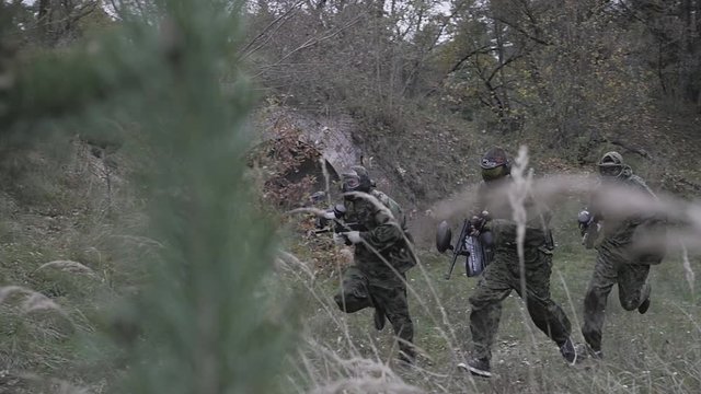 hree men of paintball players run in the forest in slow motion