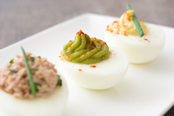 Variety of stuffed eggs with avocado and tuna on wooden table