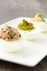 Variety of stuffed eggs with avocado and tuna on wooden table