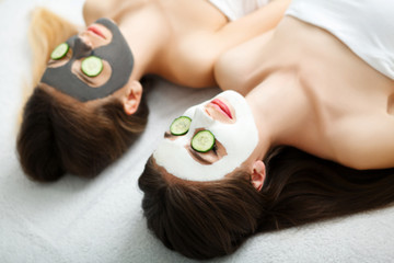 Obraz na płótnie Canvas Home spa. Two women holding pieces of cucumber on their faces lying the bed.