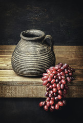 Classic still life with vintage pottery Jar placed with red grapes on rustic wooden background