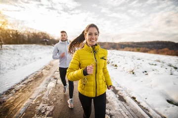 Foto op Plexiglas Joggen Mooie gelukkige actieve runner meisje joggen met haar persoonlijke knappe trainer op een besneeuwde weg in de natuur.