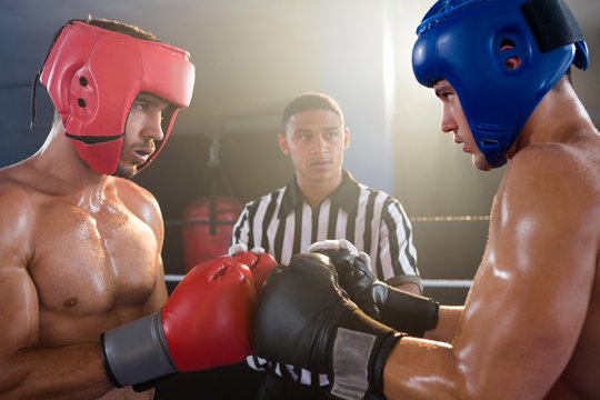 Referee looking at male boxers punching gloves