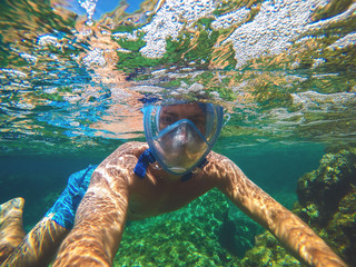 Underwater close selfie photo of a young sporty man with a snorkelling mask swimming in the...