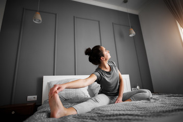 Healthy sporty shape middle aged woman doing seated yoga poses on the bed in the morning.