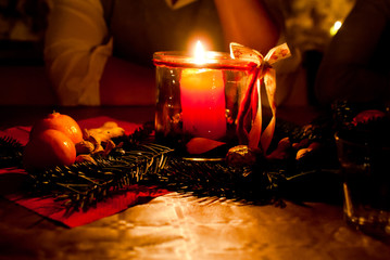rote Kerze in einem Glas als Tischschmuck auf einer Weihnachtsfeier mit Menschen im Hintergrund