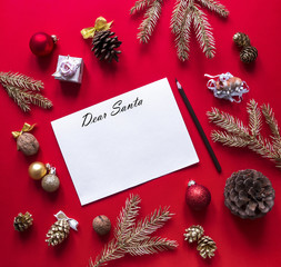 Fototapeta na wymiar on a red raspberry background, New Year and Christmas decorations and spruce gold branches are arranged in a circle, and in the center lies a white sheet with a letter to Santa Claus and a pencil