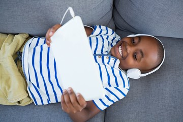 High angle view of boy using digital tablet while listening to