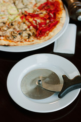 Pizza cutter on white plate. Round knife with pizza on background.