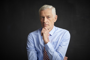 Elderly man portrait. An executive senior man wearing shirt and tie while sitting at isolated black...
