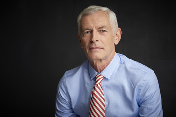 Elderly man portrait. An executive senior man wearing shirt and tie while sitting at isolated black...