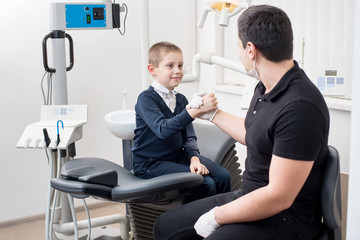 Pediatric dentist shake hands with young boy, congratulate patient for a successful treatment in dental office. Dentistry. Dental equipment