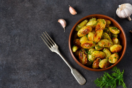 Young fried potatoes with garlic and dill on a black background