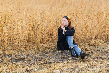 Naklejka na ściany i meble Portrait of a young brunette woman in black coat on a background of golden soybeans field, autumn outdoors