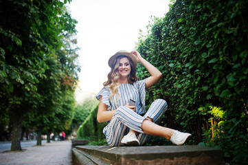 Portrait of a stunning young woman in striped overall sitting in the park and listening to the music with her earphones on.