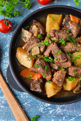 Meat goulash with vegetables, potatoes and mushrooms on concrete, grunge background