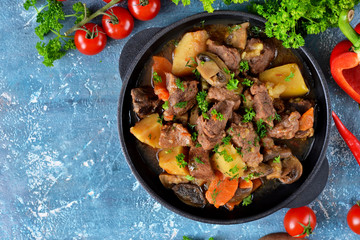 Meat goulash with vegetables, potatoes and mushrooms on concrete, grunge background