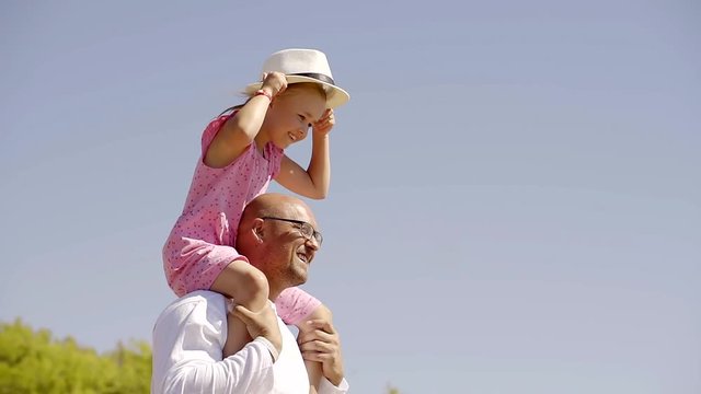 weekend dad with glasses and daughter play with a hat on a Sunny day, a father carries a child on his shoulders. to dissolve hands in the parties