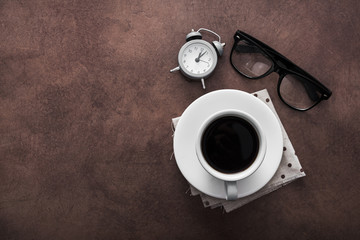 Cup of coffee with alarm clock on table and black glasses