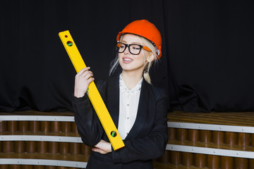 Beautiful blonde businesswoman with application tier at loft office in orange construction helmet and suit.