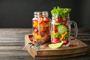 Jars with vegetable and fruit salads on wooden board