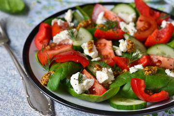 Vegetable salad with tomatoes, spinach and feta cheese on a concrete background.