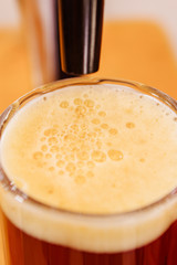 Close up of a glass of beer with foam and beer tap pouring, beer serving in a restaurant or pub, in a blurred background