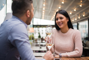 Cheerful couple drinking wine in cafe and having conversation.