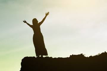 Silhouette of woman praying on mountain cliff - Concept about freedom, faith and celebration