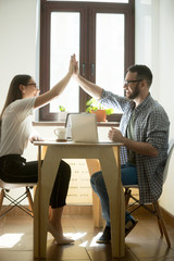 Millennial colleagues giving high fives while finishing working project in business office. Two happy successful young managers, winning concept. Vertical image