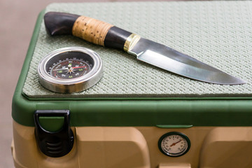 A hunting knife and a compass lie on a box for fishing.