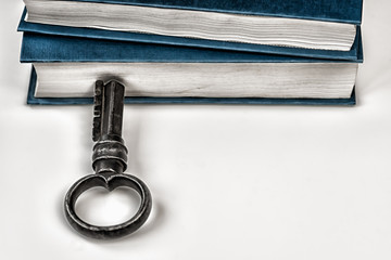 On a white table are collected paper books. Nearby there is an antique metal key. A symbol of knowledge and wisdom.