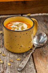 Pumpkin and carrot soup with cream on wooden background