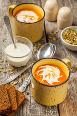 Pumpkin and carrot soup with cream on wooden background
