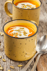 Pumpkin and carrot soup with cream on wooden background