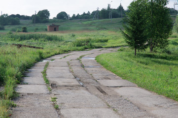 Fototapeta na wymiar Old concrete road leaving far into the distance among meadows