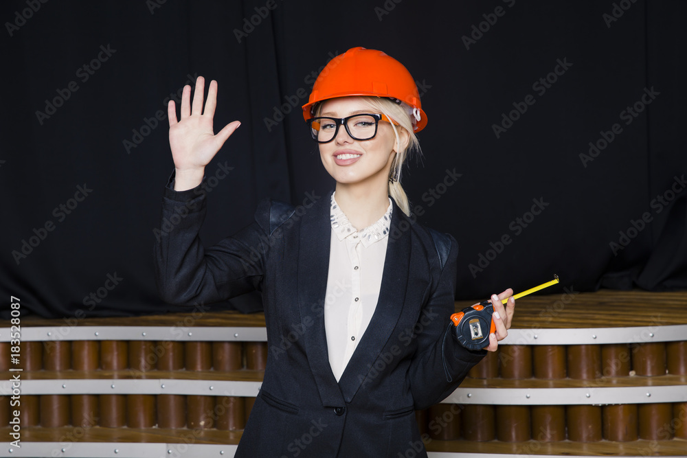 Wall mural beautiful blonde businesswoman with tape measure at loft office in orange construction helmet and su