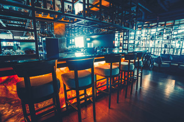 Barteller in de donkere nachtachtergrond met stoelen in leeg comfortabel luxerestaurant. Concept van pubcultuur en drinken. Diverse alcoholflessen, achterlicht. Vintage blauw retro kleurfilter