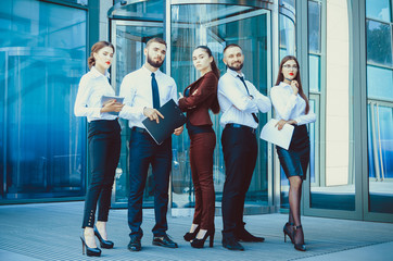 Young office workers on the background of a multi-storey glass building. Five managers. Teamwork. Office. A group of people. Exchange Traders